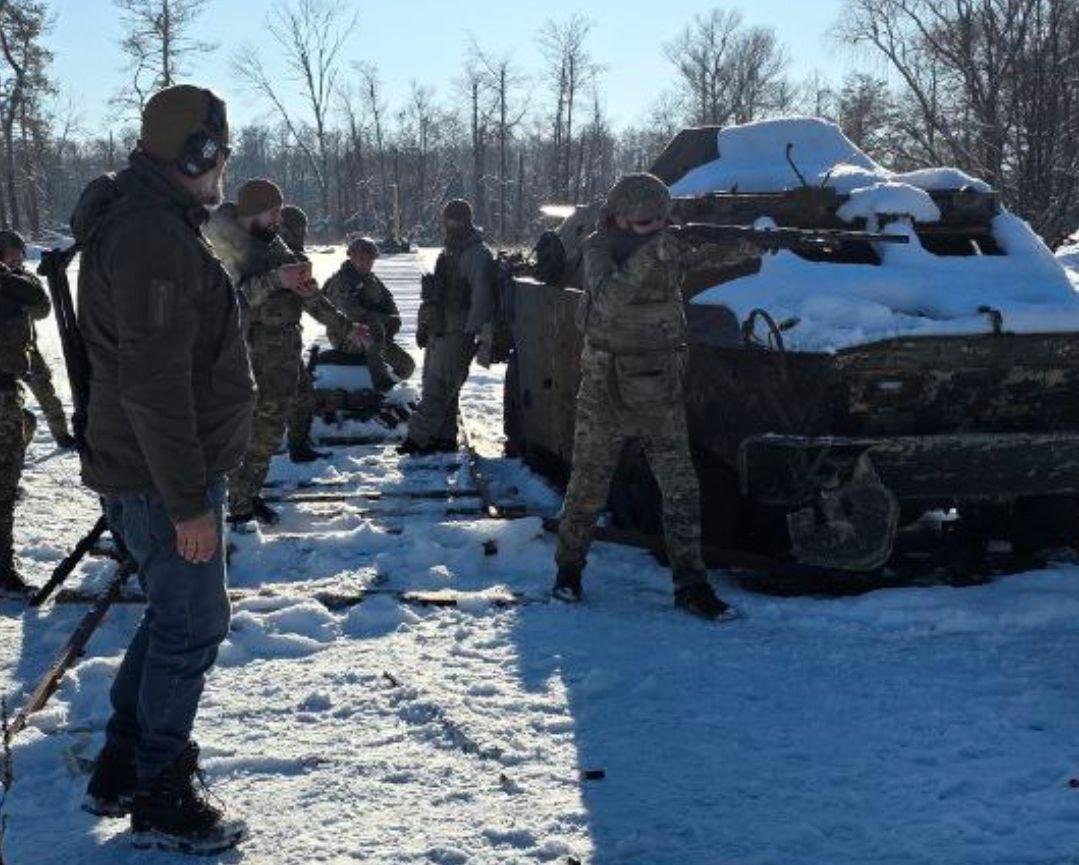 Ukrainian soldiers conducting shotgun exercises next to a wrecked armored vehicle
